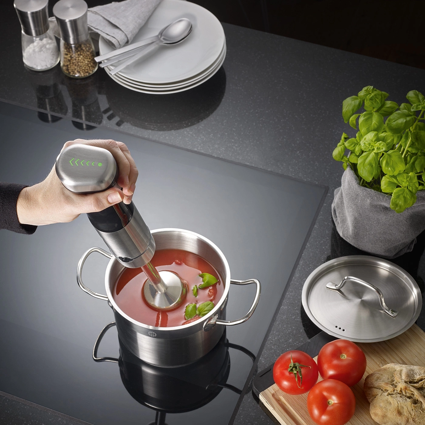 Person blending tomato soup with an immersion blender in a pot.