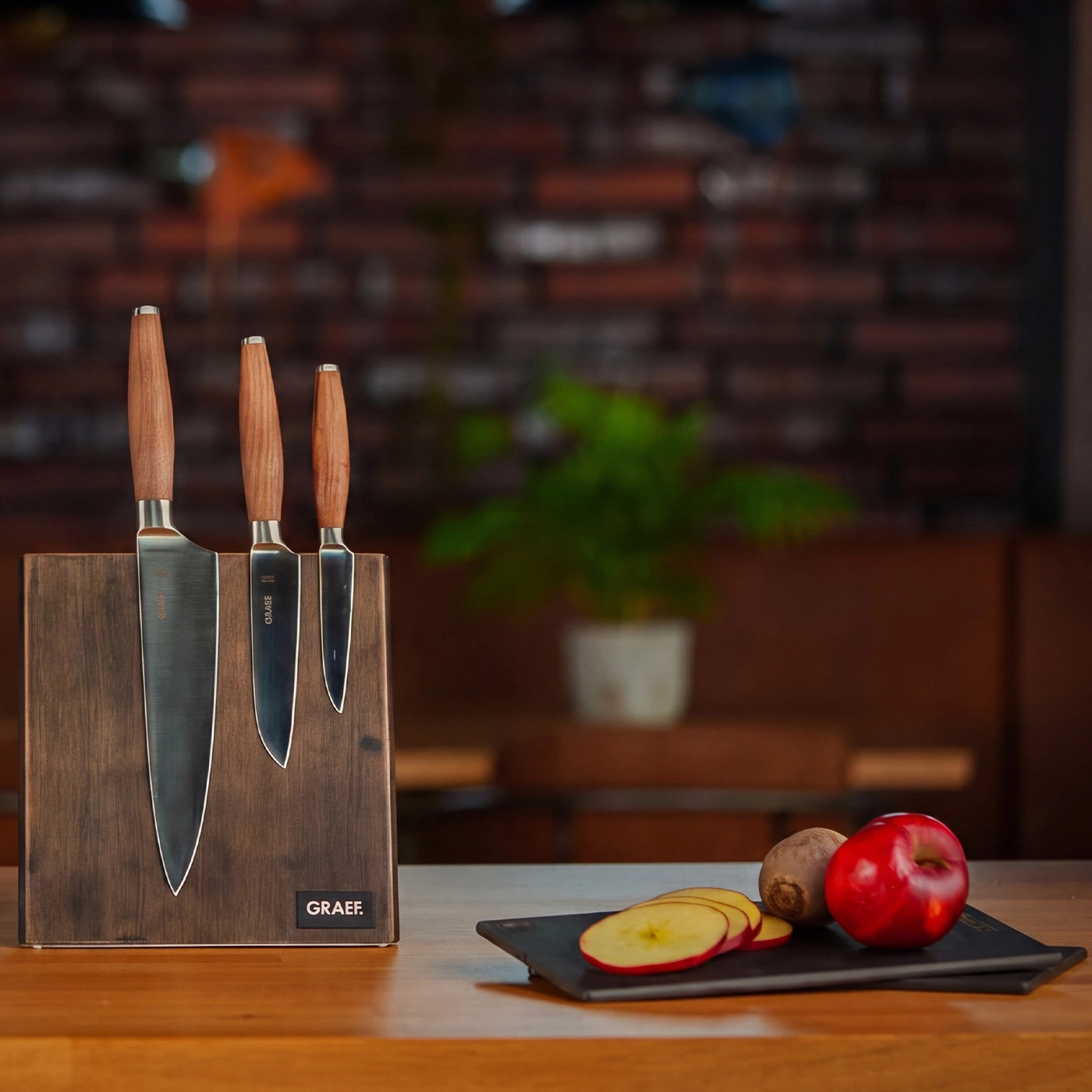 Un bloc à couteaux en bois avec trois couteaux et des fruits sur une table.
