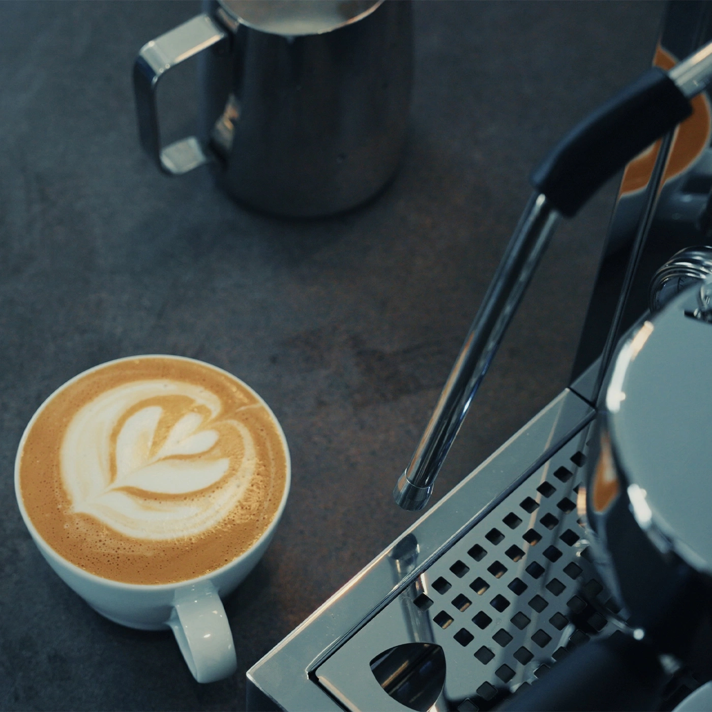 Une tasse de café latte art à côté d'une machine à expresso et d'un pichet à lait.