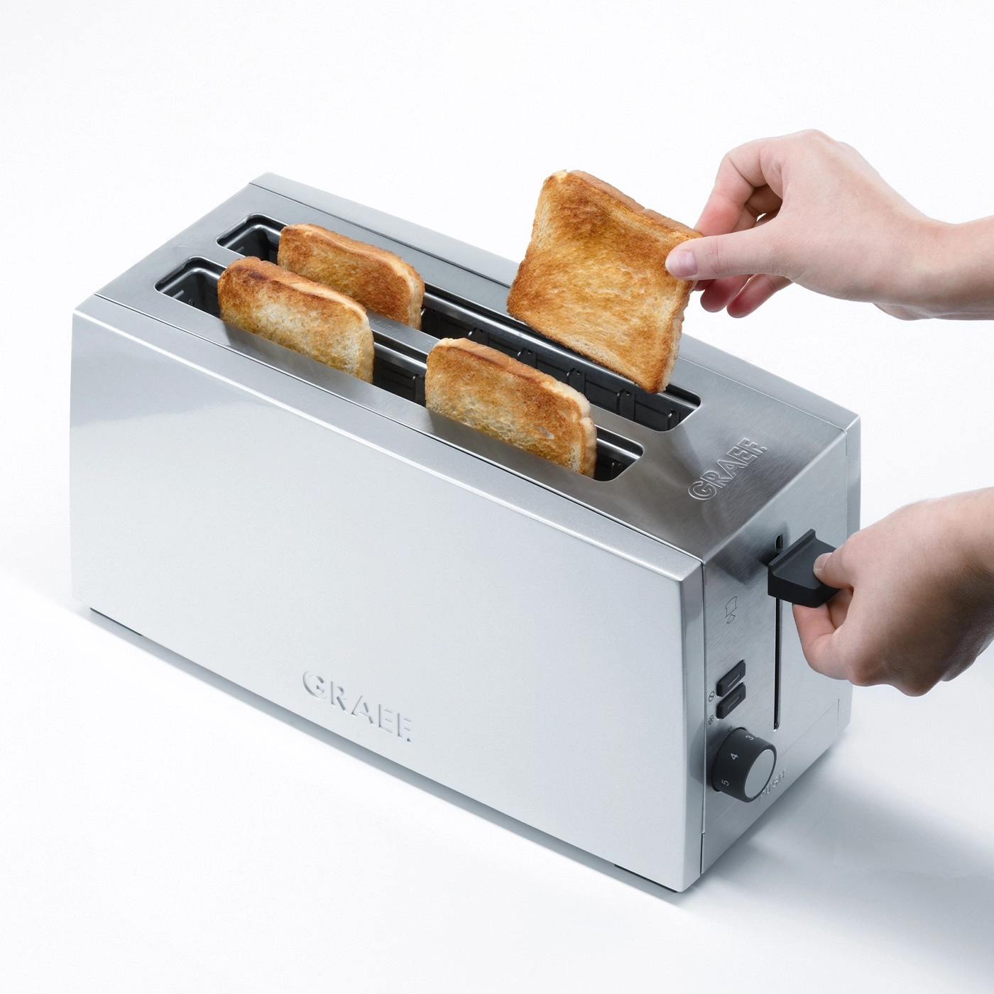 Toaster with toast, hand removing toast, silver appliance, GRAEF brand name.