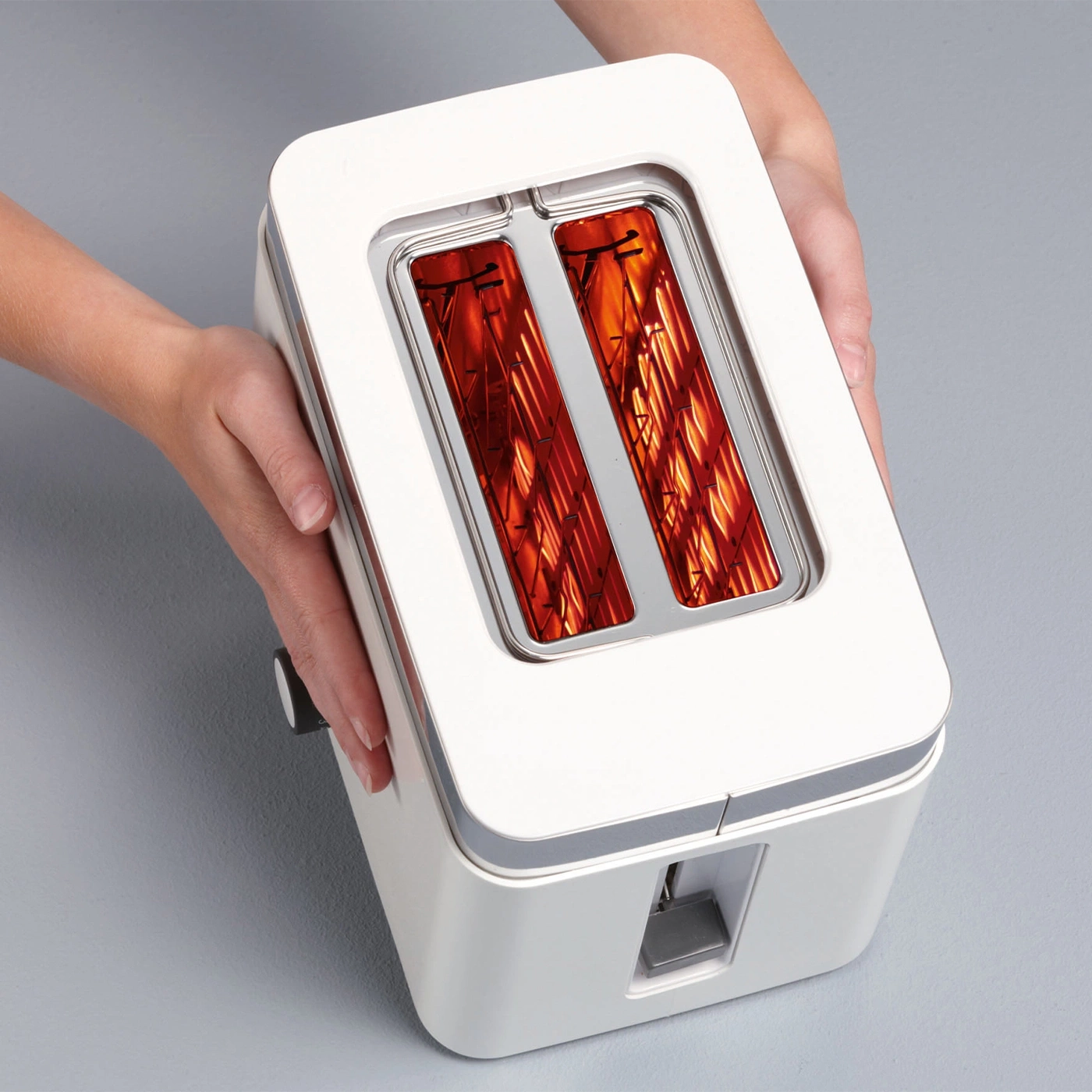 White toaster with two slots held by hands on a gray background, heating up.
