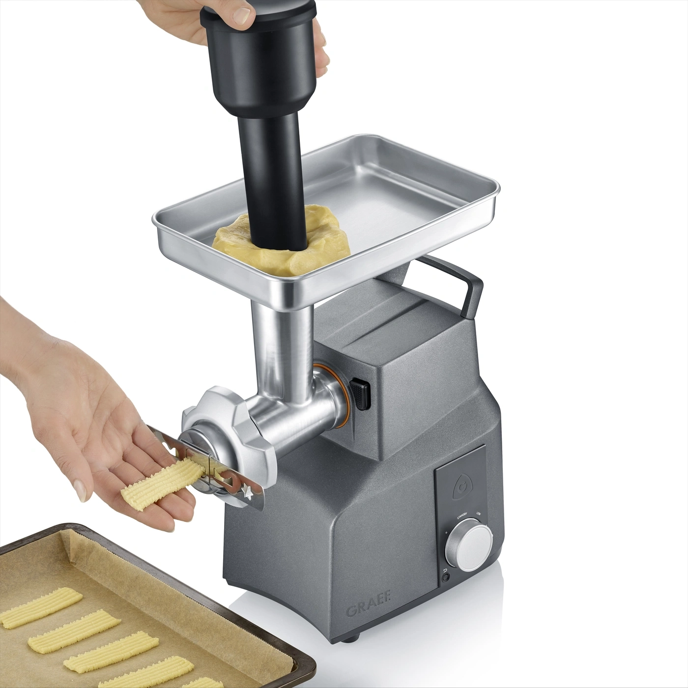 Una mano spinge l'impasto in una pressa per biscotti, formando biscotti su una teglia.