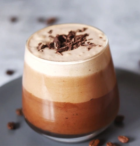 Three-layered coffee drink with chocolate shavings on a gray plate