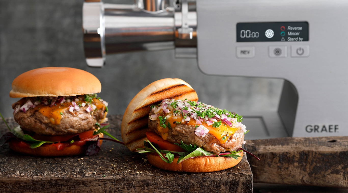 Hamburger con formaggio e cipolle vicino al tritacarne, su tavola di legno