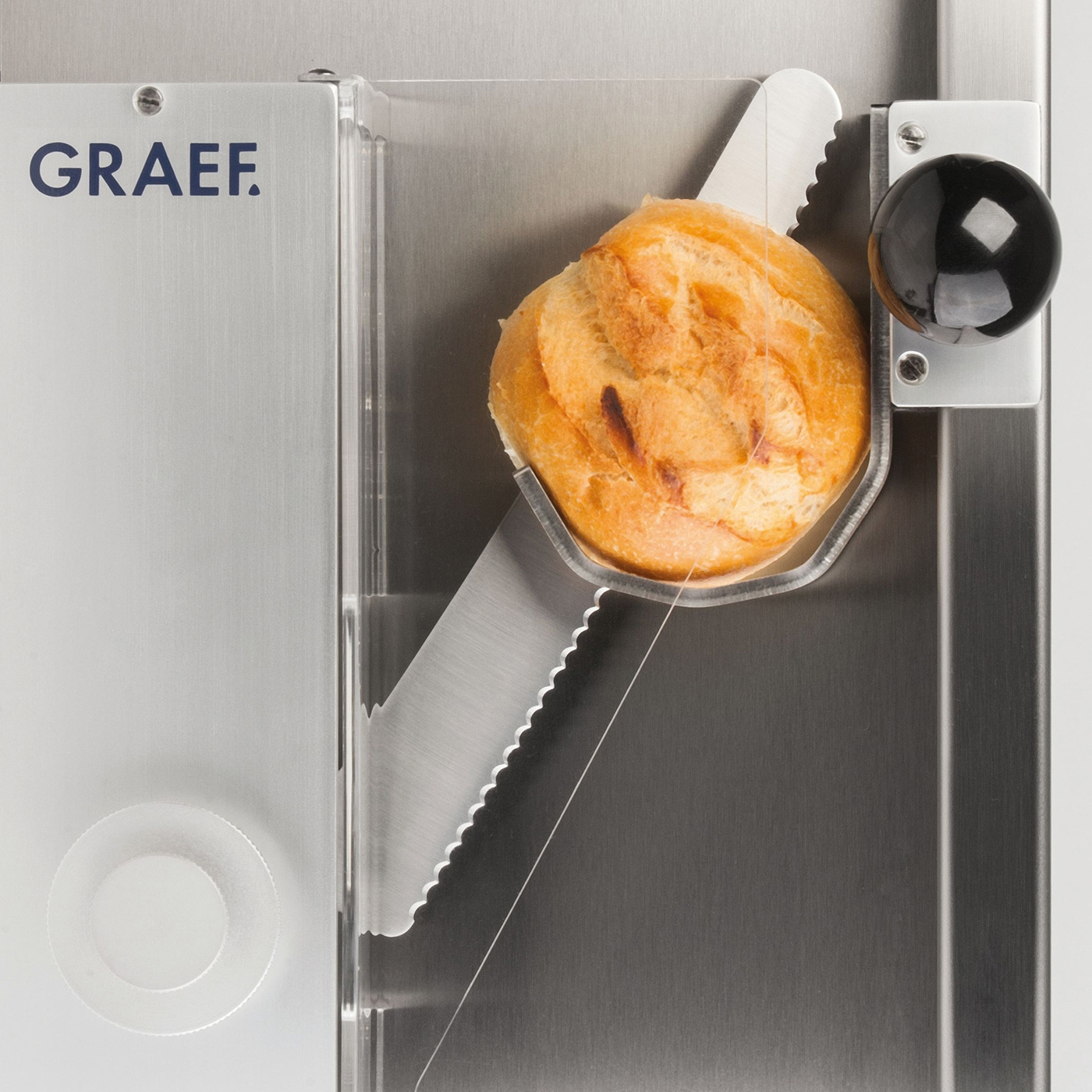 Bread in a slicer. GRAEF logo. Close-up. Stainless steel. Food preparation.