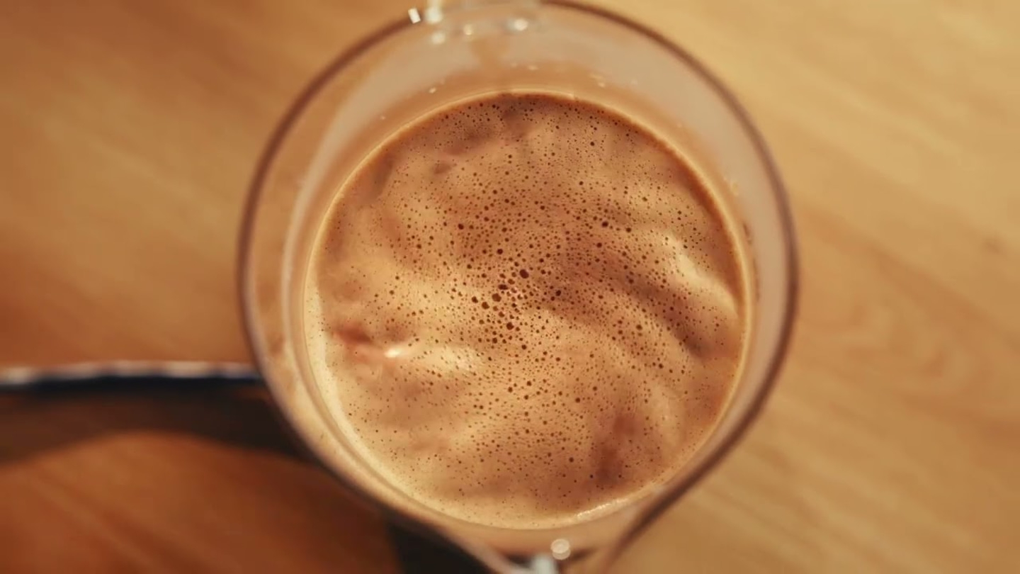 Café dans un verre, vu de dessus, sur une table en bois avec des bulles
