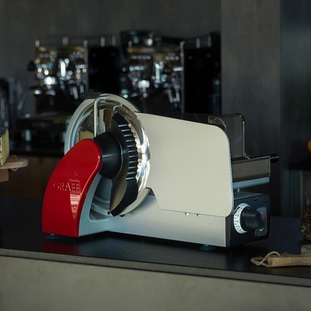 Close-up of a red and silver meat slicer on a countertop in a cafe
