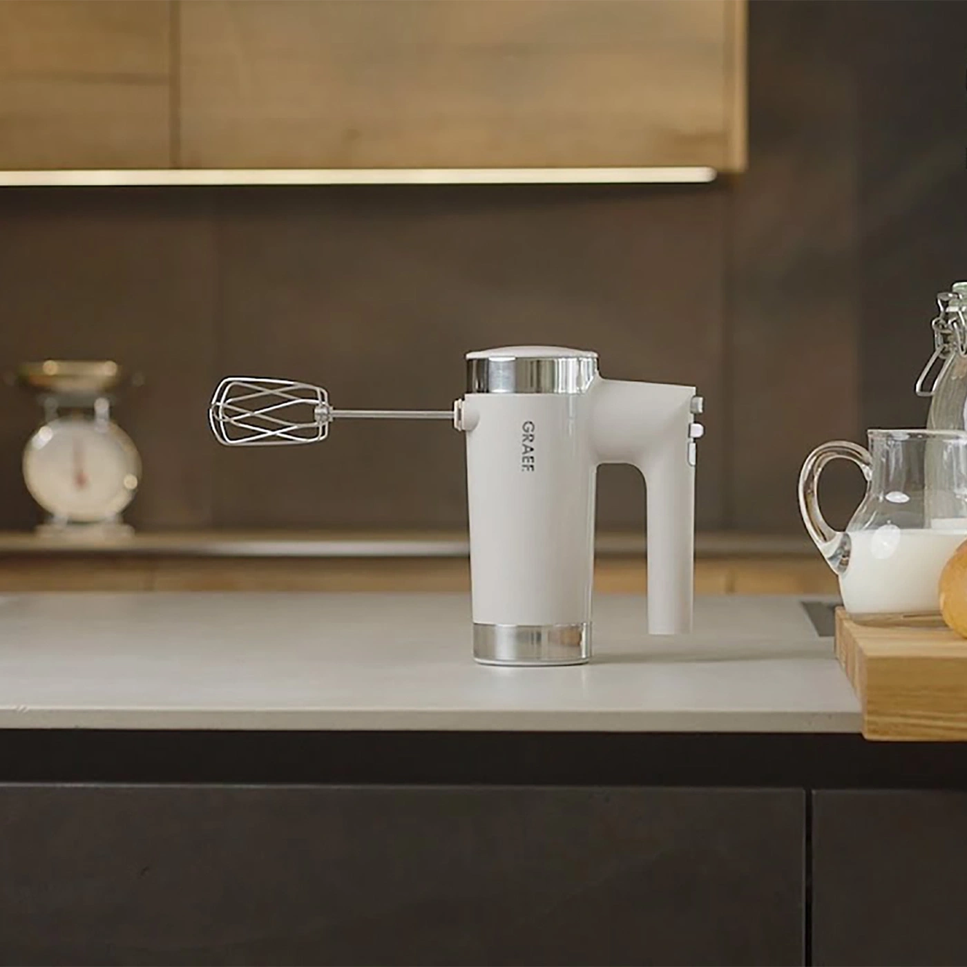 Uno sbattitore elettrico bianco è appoggiato sul piano di lavoro della cucina accanto a una caraffa di latte.