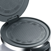 Open waffle maker with detailed baking surfaces and silver rim.