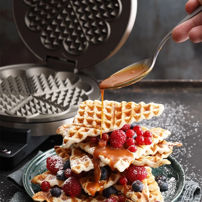 Waffle con frutti di bosco e sciroppo versati da una mano con un cucchiaio.
