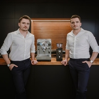 Due uomini posano con macchina da caffè e macinacaffè in cucina.