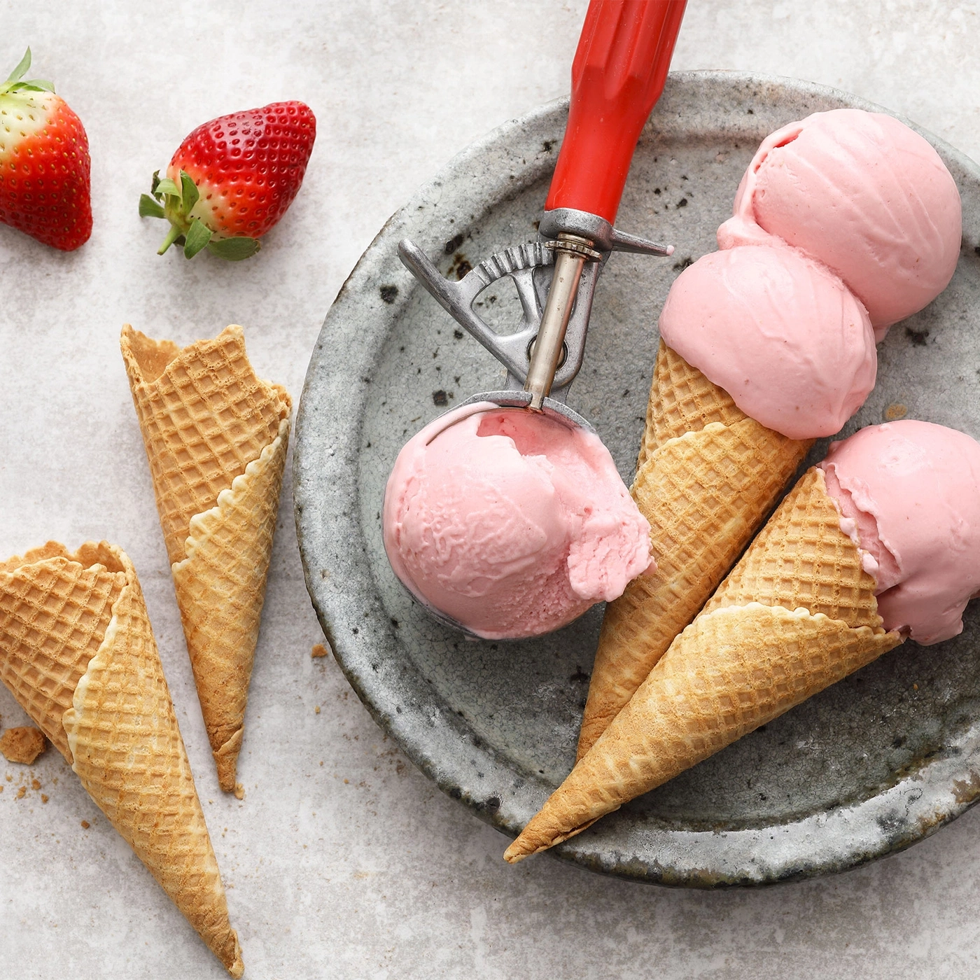 Glace à la fraise dans des cornets à gaufrette sur une assiette avec une cuillère et des fraises.