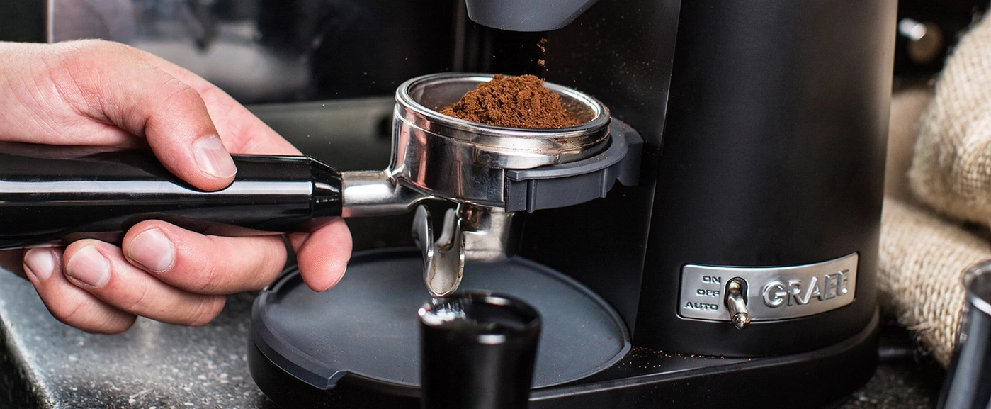 Gros plan d'une personne remplissant un porte-filtre de mouture de café à l'aide d'un moulin à café.