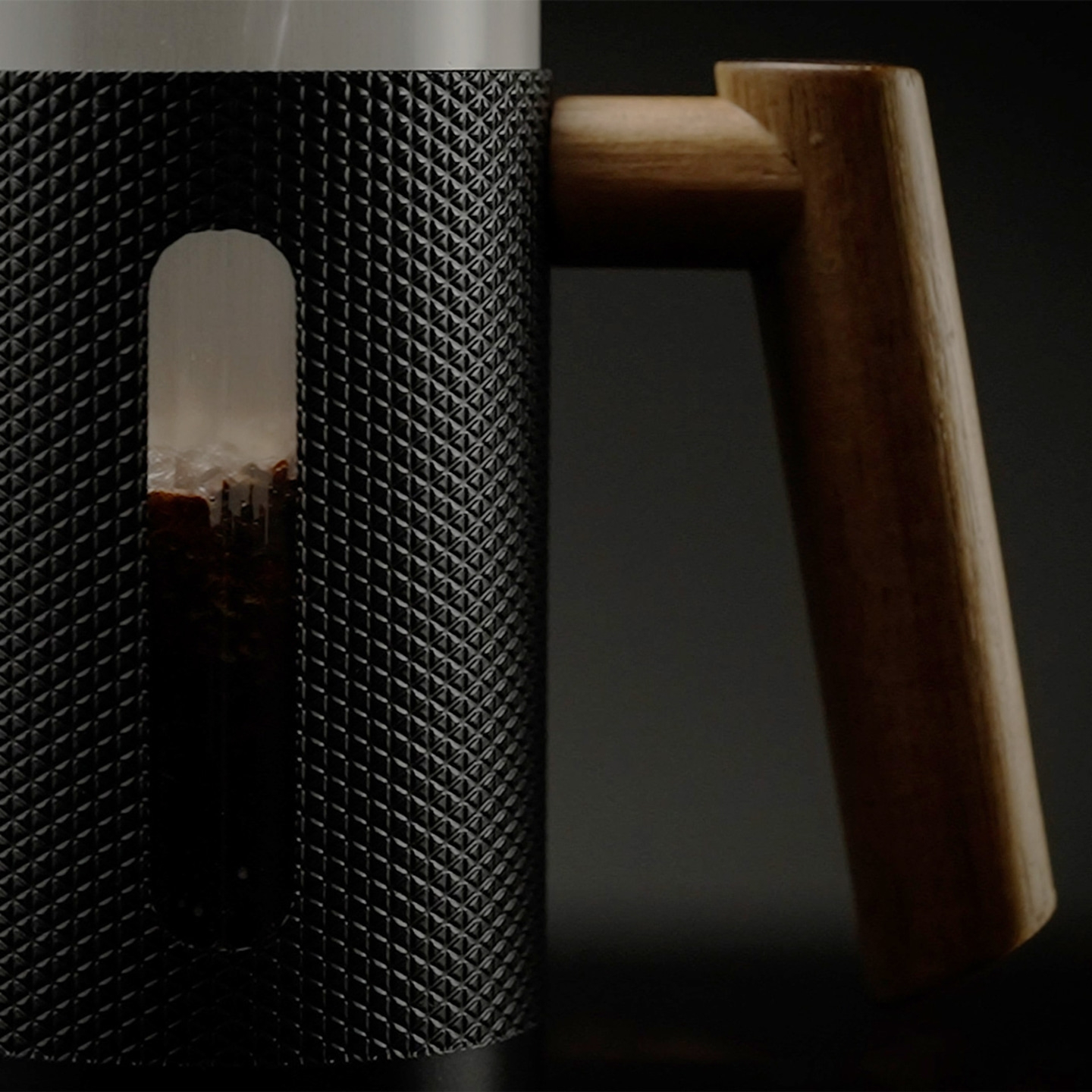 Close-up of a black coffee maker with a wooden handle and visible coffee grounds.