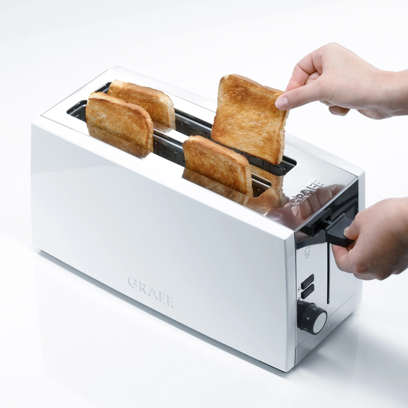 Une main retire du pain grillé d'un grille-pain blanc avec quatre tranches de pain grillé.