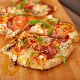 Primo piano di pizza con pomodori, formaggio ed erbe aromatiche su tagliere di legno