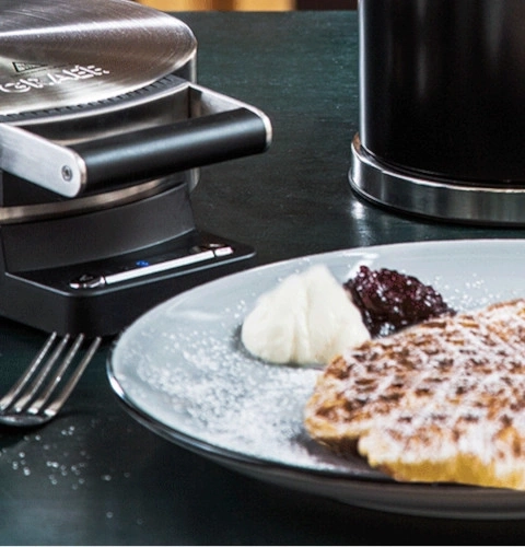 Macchina per waffle con waffle, panna e marmellata su un piatto