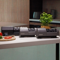 Three GRAEF knife sharpeners on a white surface with tomatoes and basil plant.