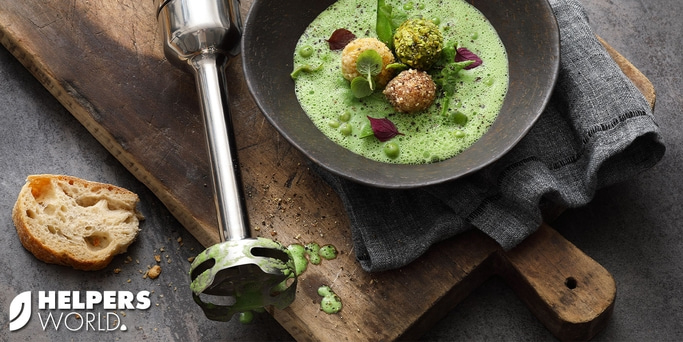 Green soup with bread, blender, and rustic wooden board. Deliciously arranged.