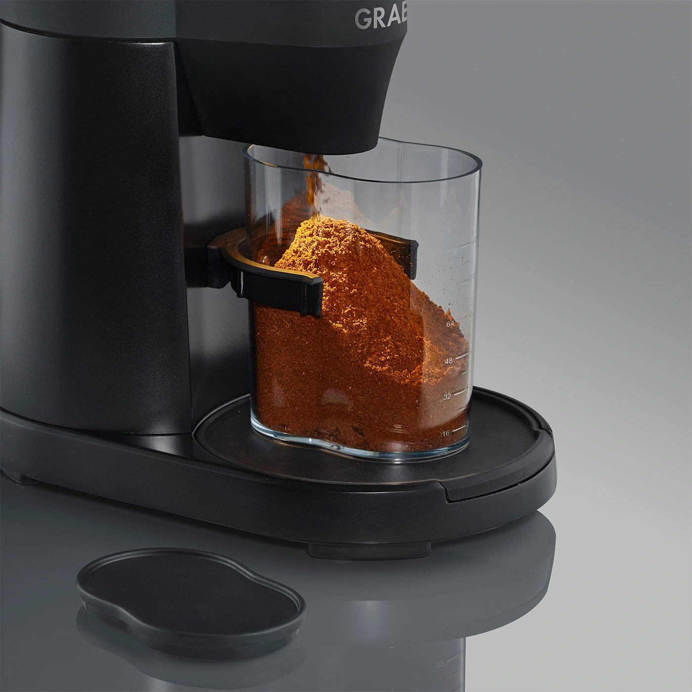 Macinacaffè con contenitore in vetro pieno di polvere di caffè, design nero, primo piano