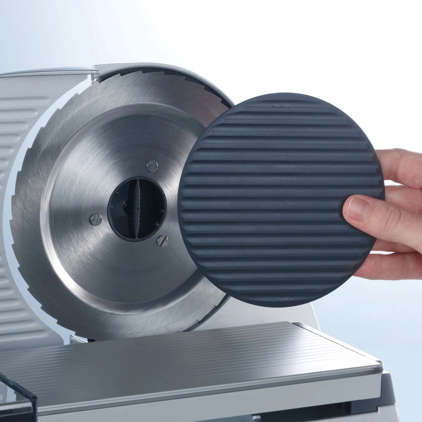 Close-up of a meat slicer with a protective device and a hand