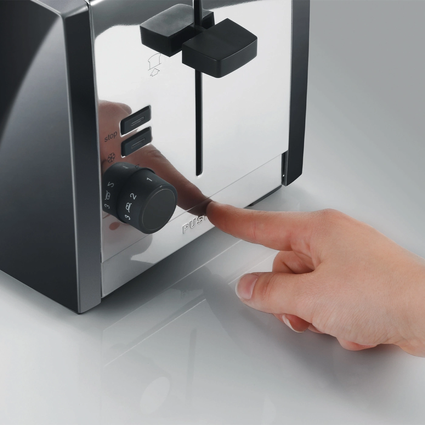 Hand presses a toaster button to make toast. Close-up shot of the appliance.