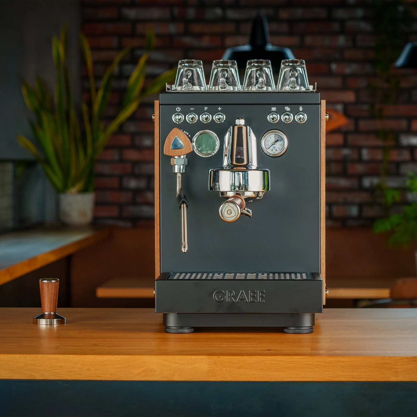 A professional espresso machine with wood accents and glasses on top.