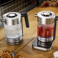 Two electric kettles on a wooden table with tea and decorations, GRAEF brand.