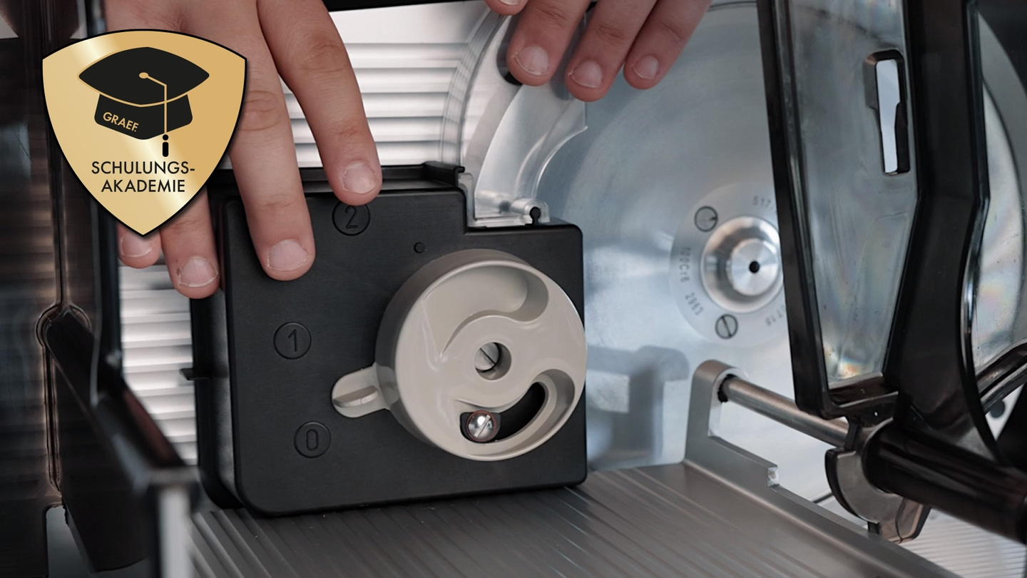 Primo piano di un'affettatrice con mani e il logo dell'accademia di formazione Graef.