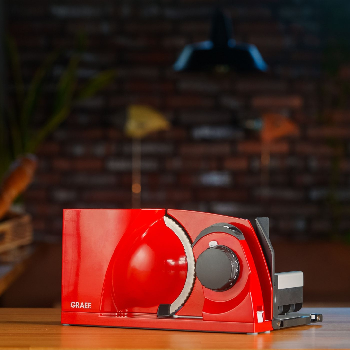 Red food slicer with GRAEF logo on wooden table in front of brick wall