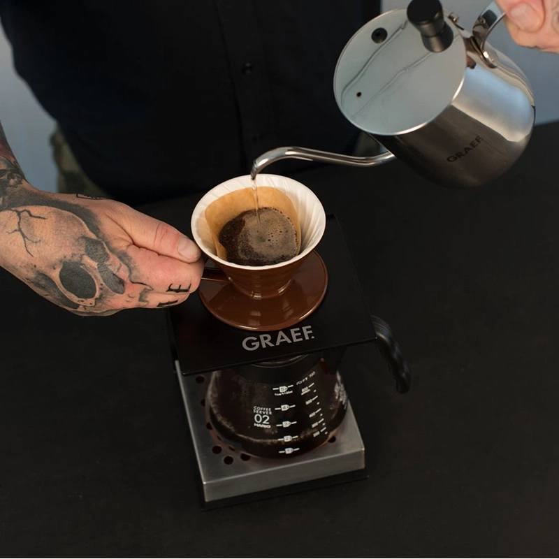 Personne versant du café dans un filtre posé sur une cafetière.