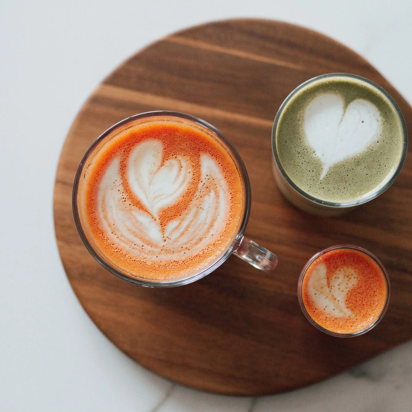 Trois boissons avec latte art sur une planche en bois, vue de dessus.