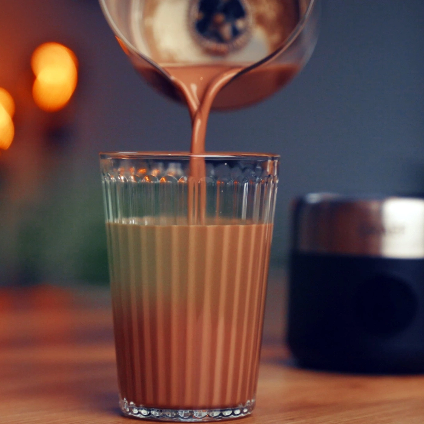 Chocolat versé dans un verre, lumières chaudes en arrière-plan.