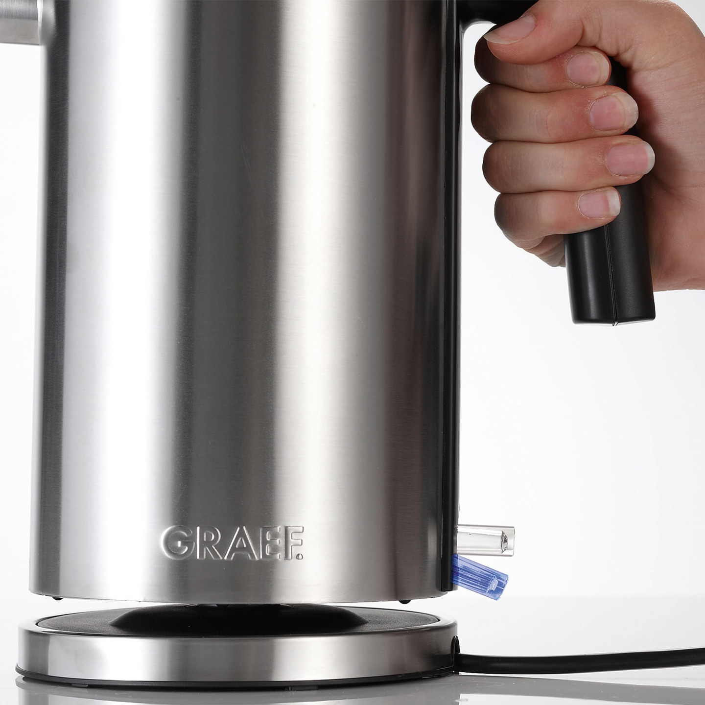 Bouilloire en acier inoxydable avec poignée et logo, tenue par une main.