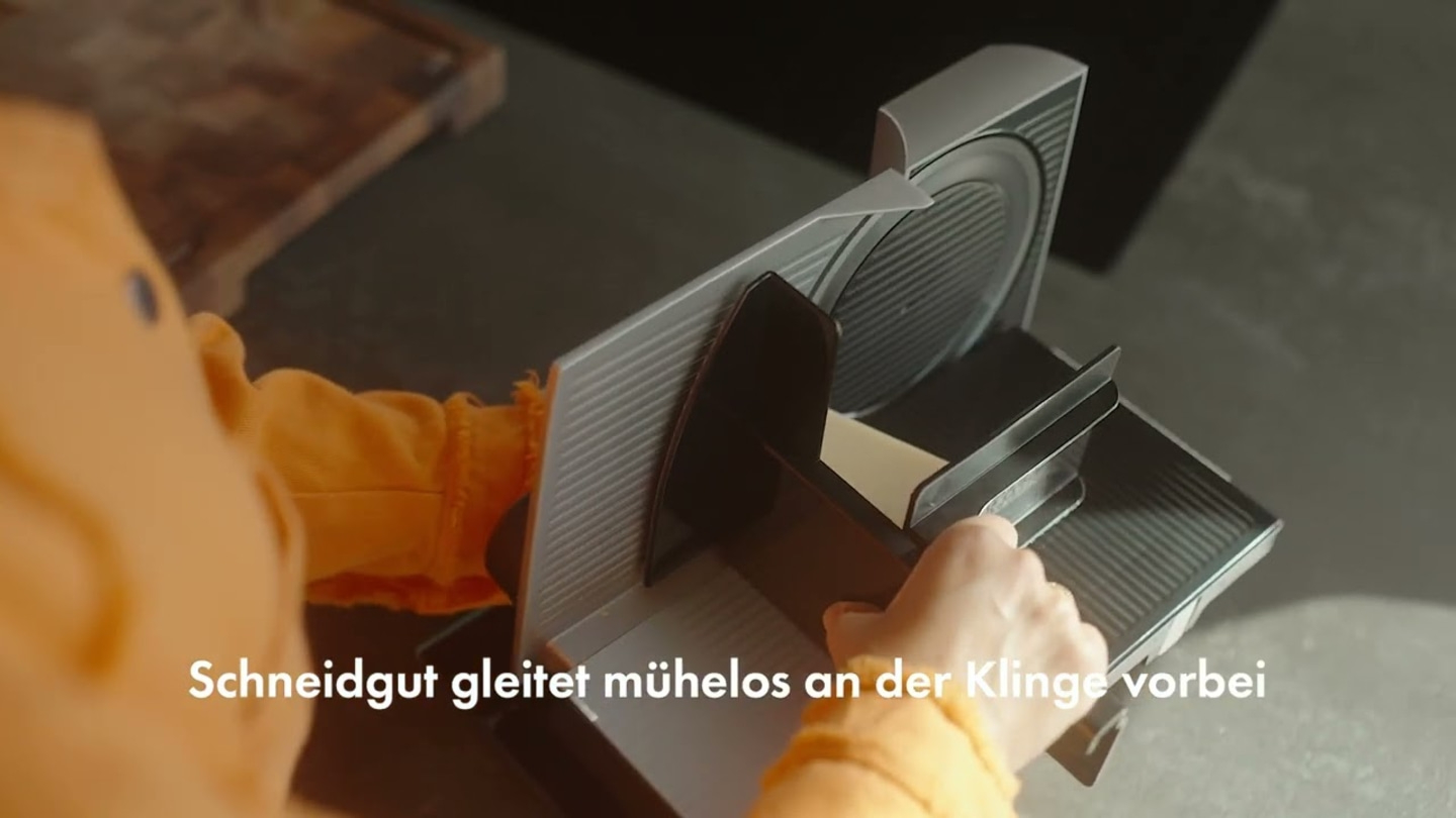 Primo piano di una persona che utilizza un'affettatrice elettrica con testo.