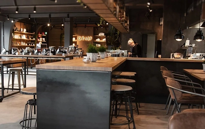 Un café avec des tabourets de bar, des tables et une personne travaillant derrière le comptoir.