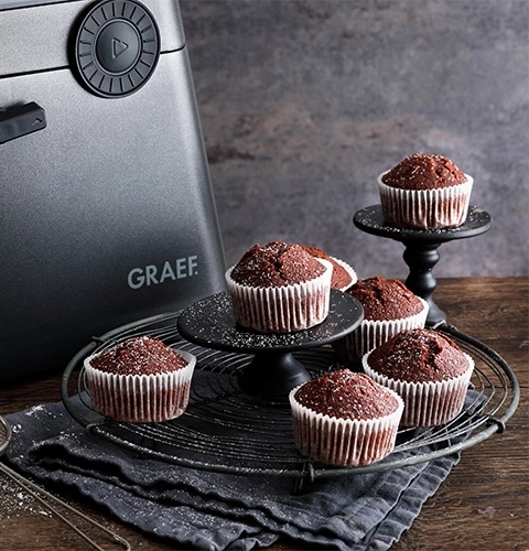 Muffin al cioccolato su una griglia e un supporto, accanto a un elettrodomestico, fotografia di cibo.