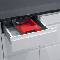 Red kitchen appliance in a drawer. Black countertop and white cabinets.