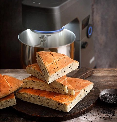 Pane con semi di sesamo, robot da cucina sullo sfondo, tagliere, primo piano