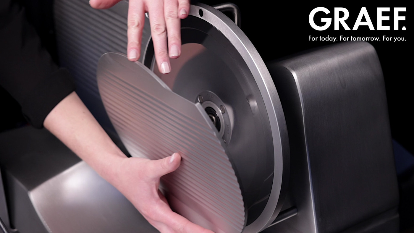 Close-up of a person operating a GRAEF slicer, with text and a black background.