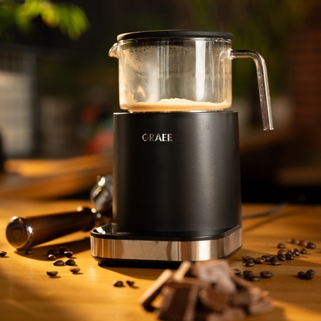 Coffee machine with glass container, coffee beans and chocolate on wooden surface