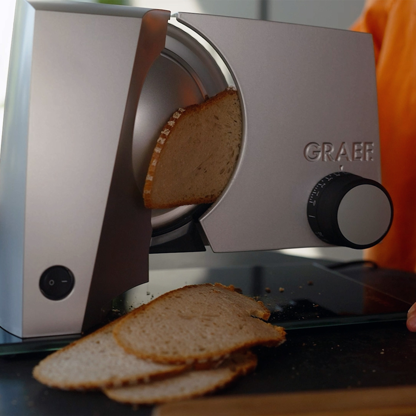 A Graef bread slicer cuts bread. Several slices of bread lie beside it.
