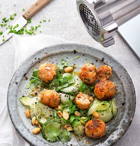Insalata di polpette con arachidi e cetrioli su un piatto con coltello e tritacarne
