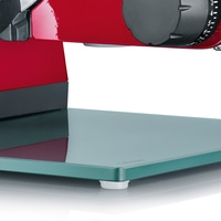 Gros plan d'une trancheuse à viande rouge avec plateau en verre et cadran de réglage.