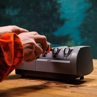 Persona che affila un coltello con un affilacoltelli su un tavolo di legno.