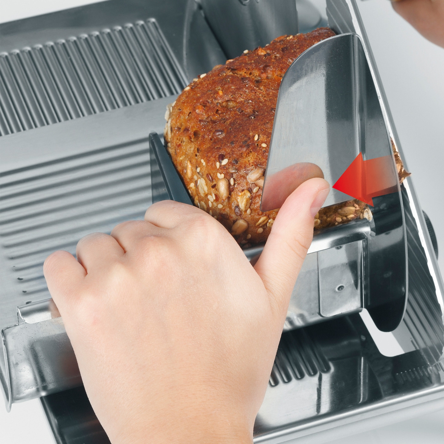 Gros plan sur une main coupant du pain avec une trancheuse à pain, flèche rouge direction.