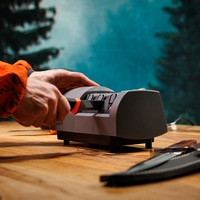 Man sharpens knife on electric sharpener in forest