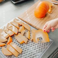 Pumpkin slices on a tray, with a whole pumpkin on a cutting board nearby