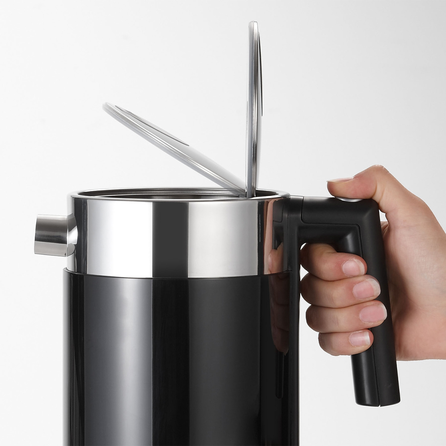 Bollitore nero con coperchio aperto tenuto da una mano, metallo lucido e plastica nera.