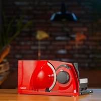 Red food slicer with GRAEF logo on wooden table in front of brick wall